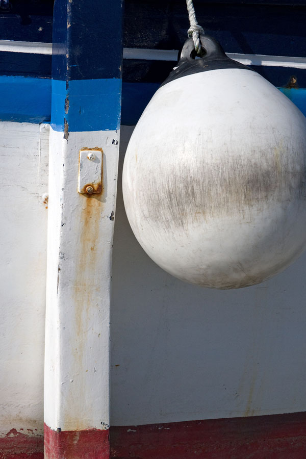 Photo, photographie de détail de coque de bateau du Finistère, bleu, rouge et blanc avec une béquille. Une grosse bouée pend au bout d'une corde ou d'un cordage @ Christophe Pluchon