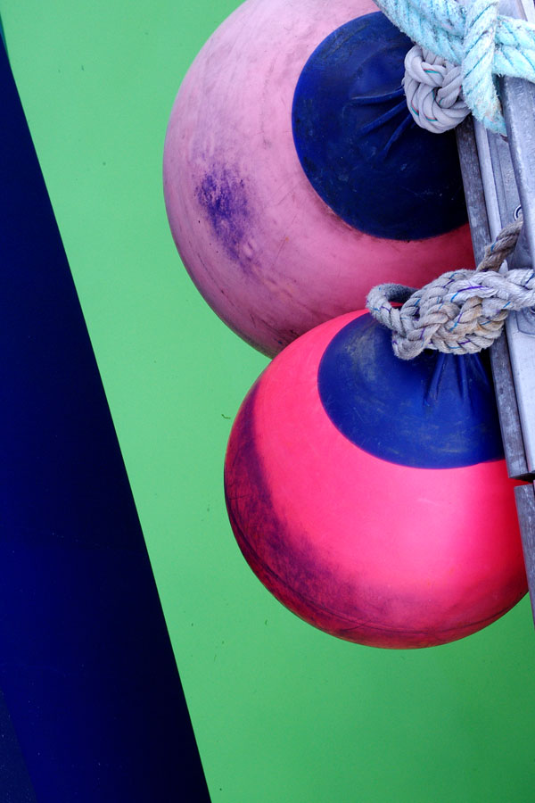 Photo, photographie de détail de coque de bateau du Finistère. Deux bouées rose et bleu d'un voilier sont retenues par une corde ou un cordage au-dessus de l'eau couleur vert @ Christophe Pluchon