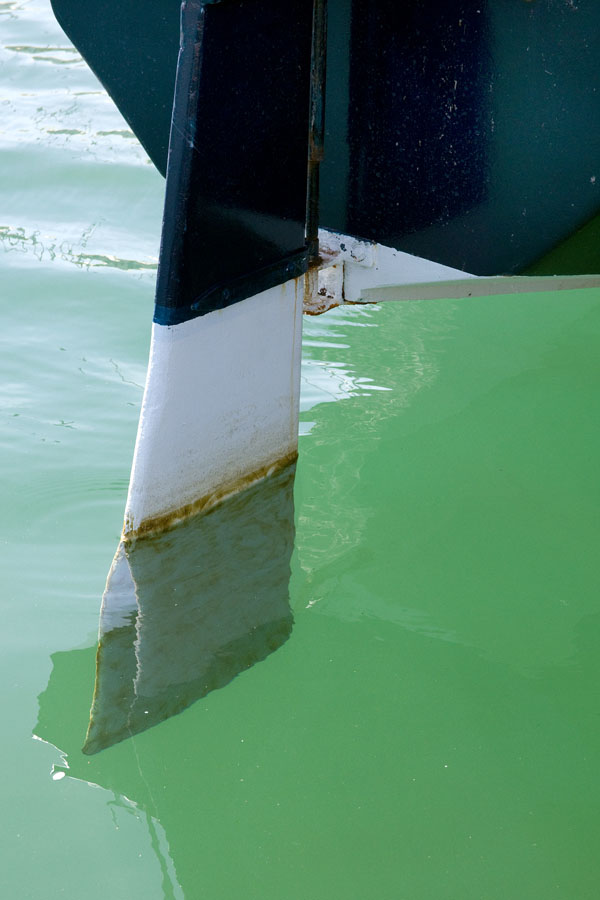 Photo, photographie de détail de coque de bateau du Finistère. Le gouvernail d'un voilier blanc et vert-bleu est dans l'eau couleur vert @ Christophe Pluchon