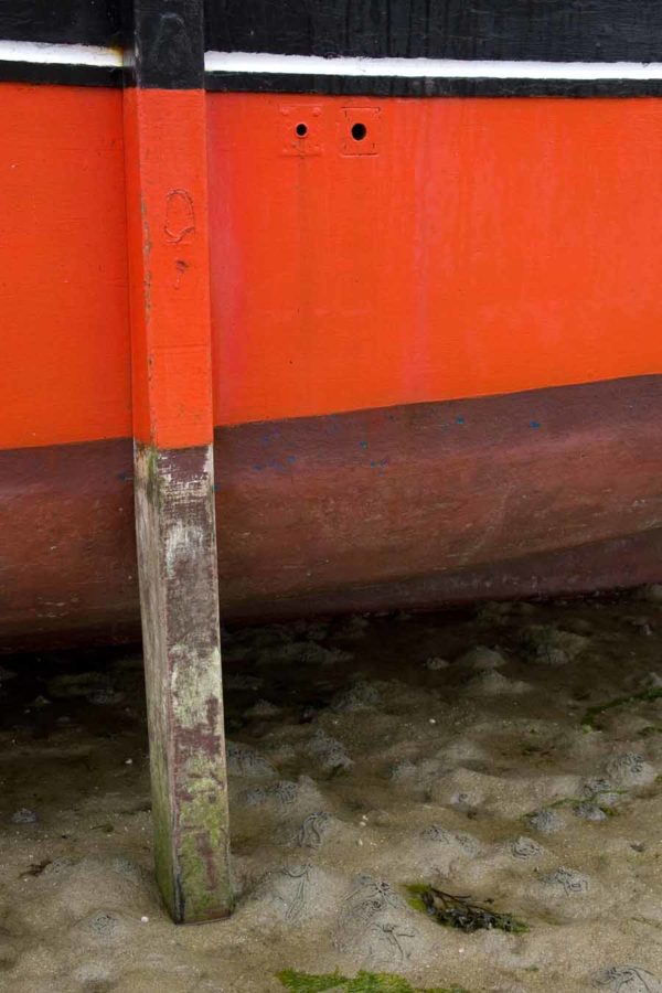 Photo, photographie de détail de coque de bateau du Finistère, orange, noir, marron, blanc, vert, avec une béquille sur le sable @ Christophe Pluchon